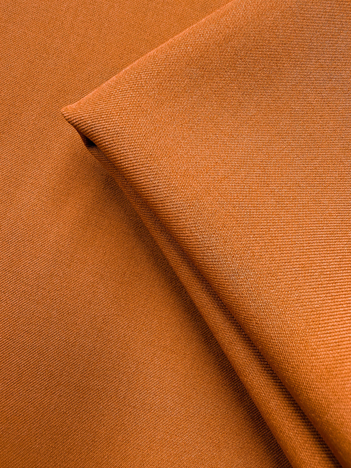 Close-up of Liquid Twill - Tomato Cream (150cm) by Super Cheap Fabrics, featuring neatly folded orange fabric with a subtle textured weave, smooth soft polyester, and fine stitching details.