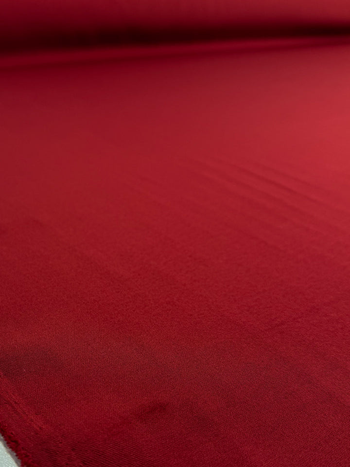 A close-up of Super Cheap Fabrics' Liquid Twill - Rythmic Red (150cm) shows the fabric laid flat, emphasizing its smooth texture and subtle sheen.