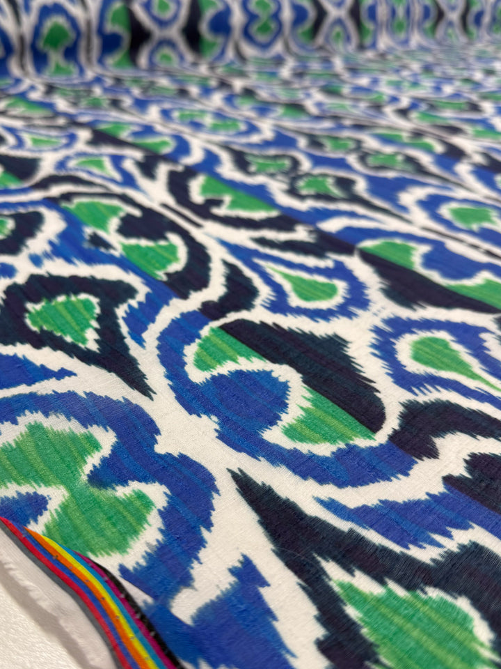 A close-up of Super Cheap Fabrics' Textured Designer Cotton - Tribal Sea (145cm): lightweight cotton with a bold blue, green, and black abstract ikat pattern on white, plus a small rainbow stripe—ideal for luxury sewing projects.