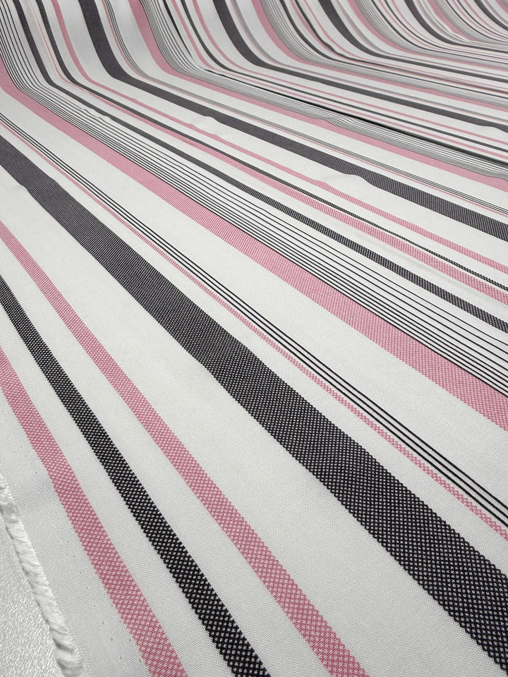 A close-up of Super Cheap Fabrics' Printed Rayon - Candy Noir Stripe (140cm), featuring lightweight, draped fabric with pink, black, white, and grey horizontal stripes forming a wave-like effect.