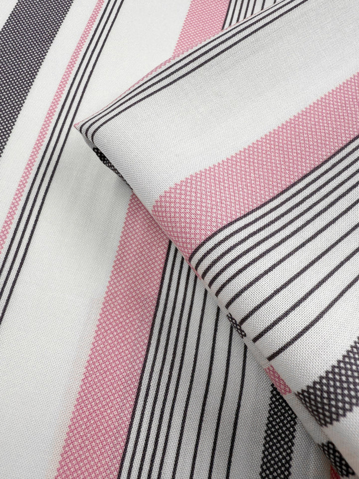 A close-up of Super Cheap Fabrics' Printed Rayon - Candy Noir Stripe (140cm), featuring lightweight rayon in pink, black, and white stripes of varying widths. Soft folds highlight its textured weave and precise stripe alignment.