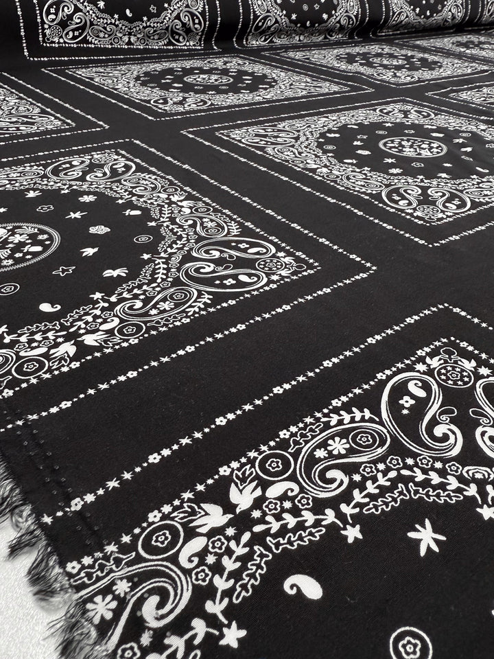 Designer Rayon - Bandana Noir - 148cm from Super Cheap Fabrics: a black lightweight rayon with repeating white paisley, floral, and geometric square prints, finished with a unique frayed trim.