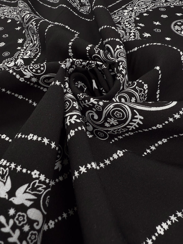 Designer Rayon - Bandana Noir by Super Cheap Fabrics features lightweight black rayon with white paisley and floral bandana patterns, gathered and twisted at the center for elegant folds and texture. Width: 148cm.