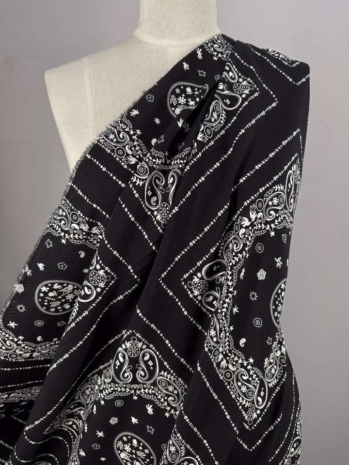 A mannequin showcases Super Cheap Fabrics' Designer Rayon - Bandana Noir (148cm), featuring lightweight black rayon with a white paisley and geometric bandana print, set against a plain light gray background.