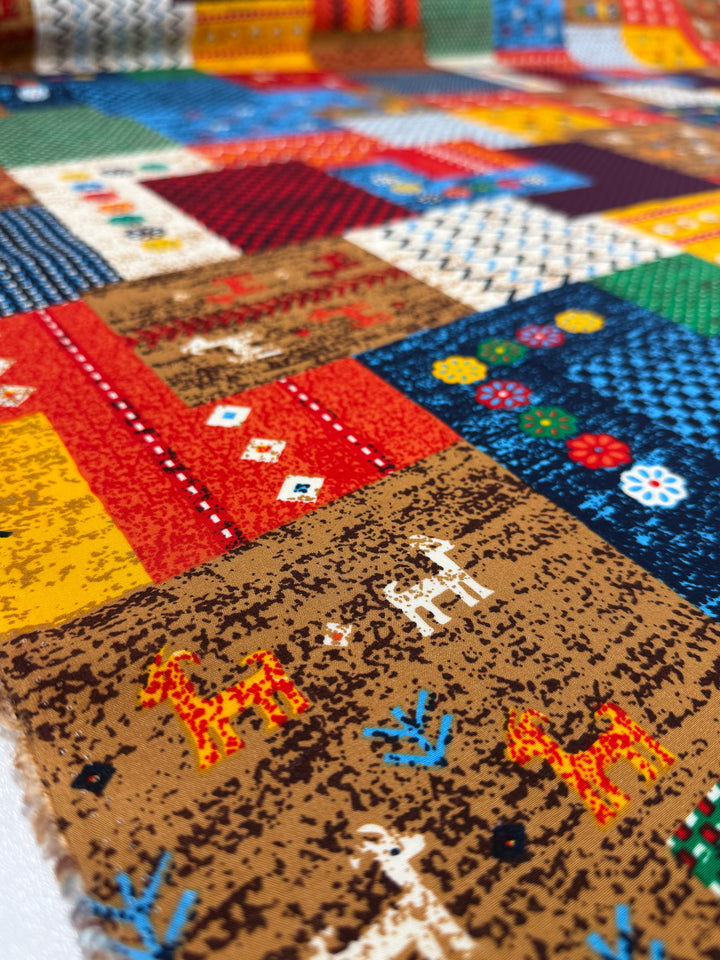 A close-up of Super Cheap Fabrics’ Designer Rayon - Andes Patchwork (147cm) shows vibrant printed rayon squares in red, blue, yellow, and brown, featuring animal and geometric patterns in a colorful patchwork.