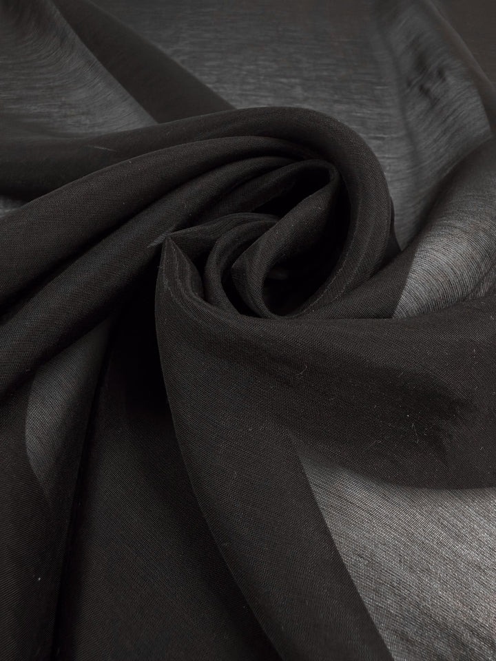 A close-up of Super Cheap Fabrics’ Designer Voile - Black - 150cm, arranged in soft folds to showcase its elegant, semi-transparent texture and smooth, lightweight finish.
