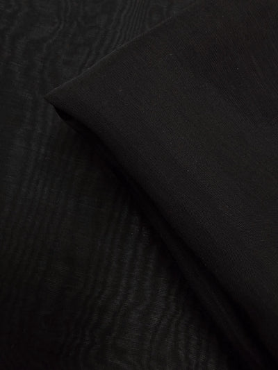 A close-up of Super Cheap Fabrics' Designer Voile - Black - 150cm displays its smooth, lightweight texture and subtle folds, with one section neatly folded over another.