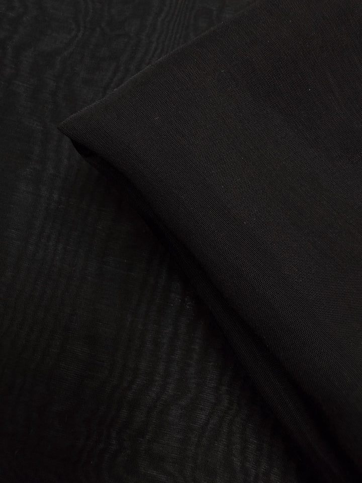 A close-up of Super Cheap Fabrics' Designer Voile - Black - 150cm displays its smooth, lightweight texture and subtle folds, with one section neatly folded over another.