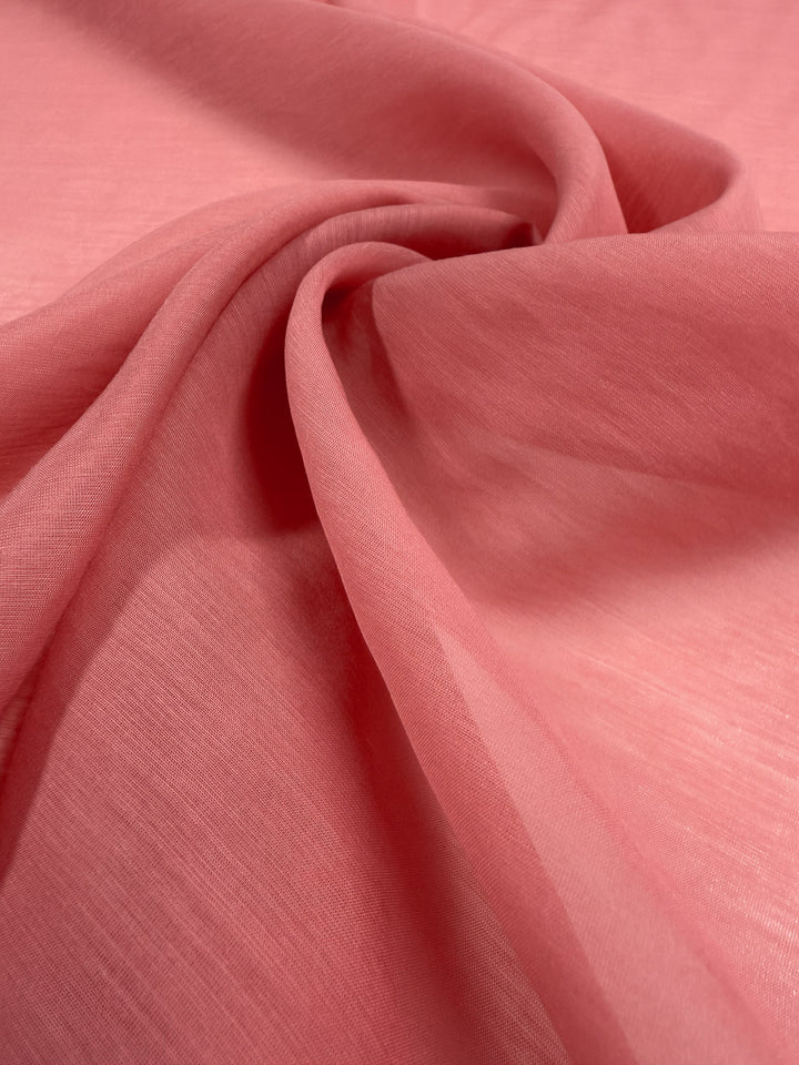 A close-up of the soft, lightweight Designer Voile - Rose of Sharon - 150cm by Super Cheap Fabrics in coral pink shows gentle folds and a slightly sheer texture, perfect for creating smooth, fluid summer dresses.