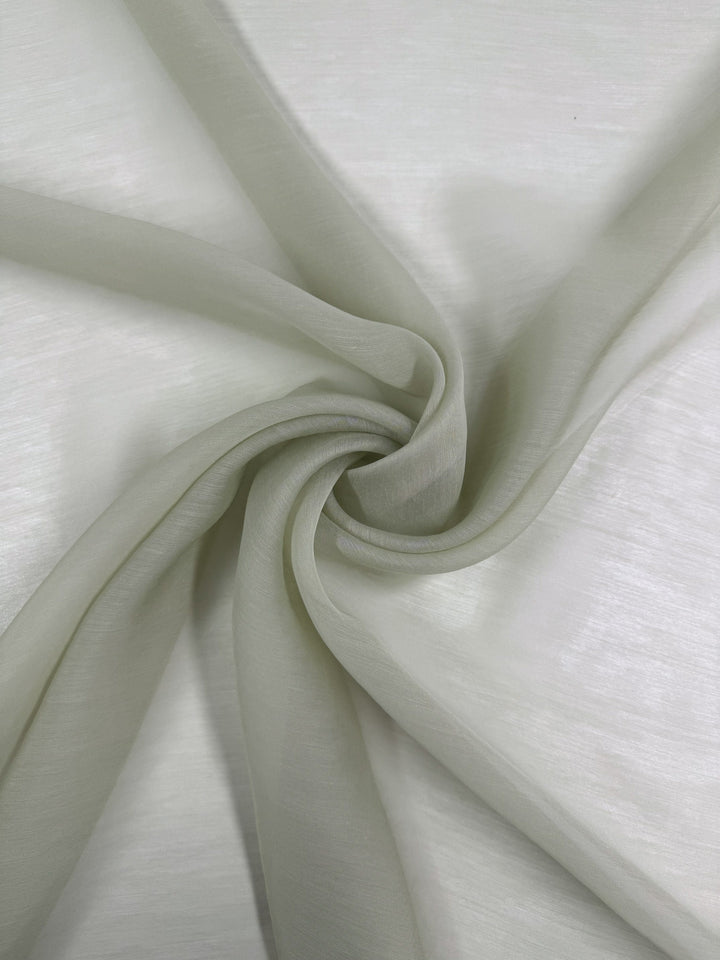 Designer Voile - White Jade - 150cm by Super Cheap Fabrics is a soft, sheer cotton nylon fabric, elegantly draped in gentle folds on a white surface for a delicate, flowing effect.