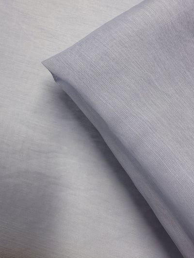 A close-up of Designer Voile - Skywriting - 150cm by Super Cheap Fabrics shows light gray, finely woven lightweight fabric with soft folds and a smooth texture—ideal for sheer curtains or designer voile applications.