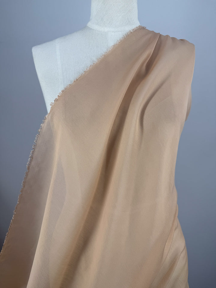 Designer Voile - Apple Blossom (150cm) by Super Cheap Fabrics, a beige sheer fabric, is draped diagonally over a white mannequin torso and displayed against a plain light gray background.