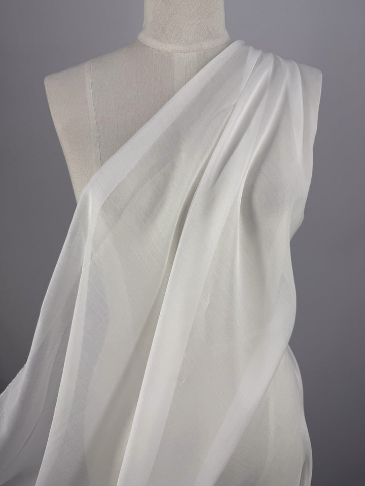 Super Cheap Fabrics' Designer Voile - White - 150cm, a lightweight sheer fabric, drapes diagonally from shoulder to opposite hip over a dress form in soft folds, set against a plain gray background.