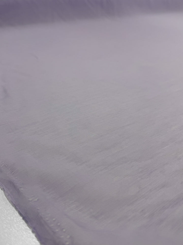 A close-up of Designer Voile - Pastel Lilac - 150cm by Super Cheap Fabrics shows its lightweight cotton texture and subtle folds, emphasizing the fabric's delicate look.