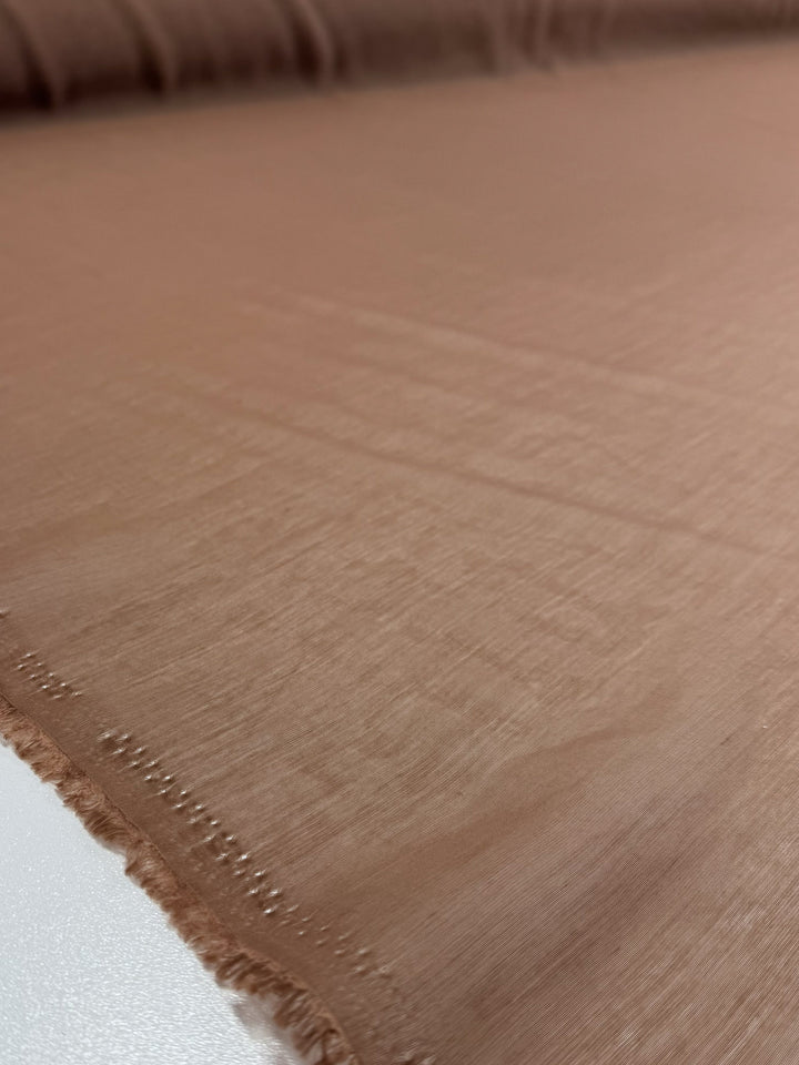 A close-up of Super Cheap Fabrics' Designer Voile - Burro - 150cm shows its extra lightweight texture and gently frayed edges, smoothly laid out on a flat surface.