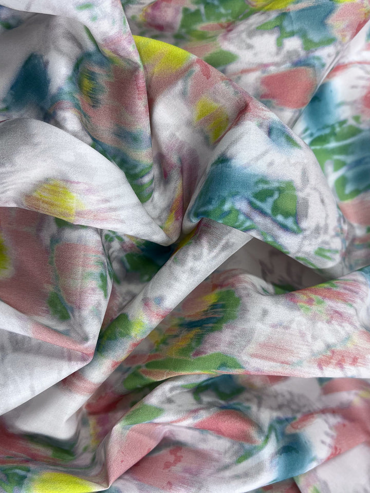 A close-up view of Super Cheap Fabrics' Printed Cotton - Terrain - 150cm showcases its lightweight cotton fabric with a colorful abstract pattern in pastel blues, pinks, yellows, and greens. The natural fibers are gently folded for a textured and flowing look.