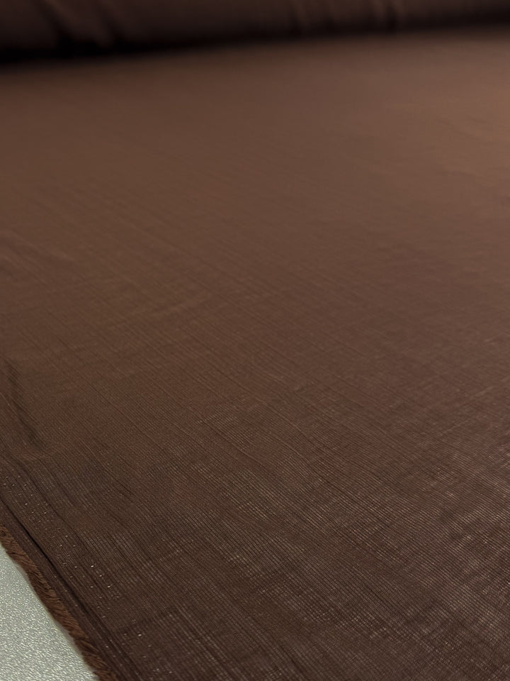 A close-up of Super Cheap Fabrics' Textured Designer Voile - French Roast (155cm) shows its brown hue, intricate weave, and smooth finish—ideal for refined summer garments.