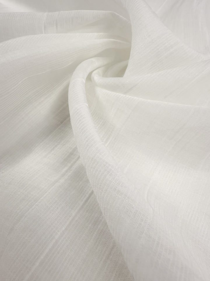 A close-up of Super Cheap Fabrics' Textured Designer Voile in Ivory (155cm), highlighting its white semi-transparent texture, subtle pattern, and delicate draping with gentle curves and lines.