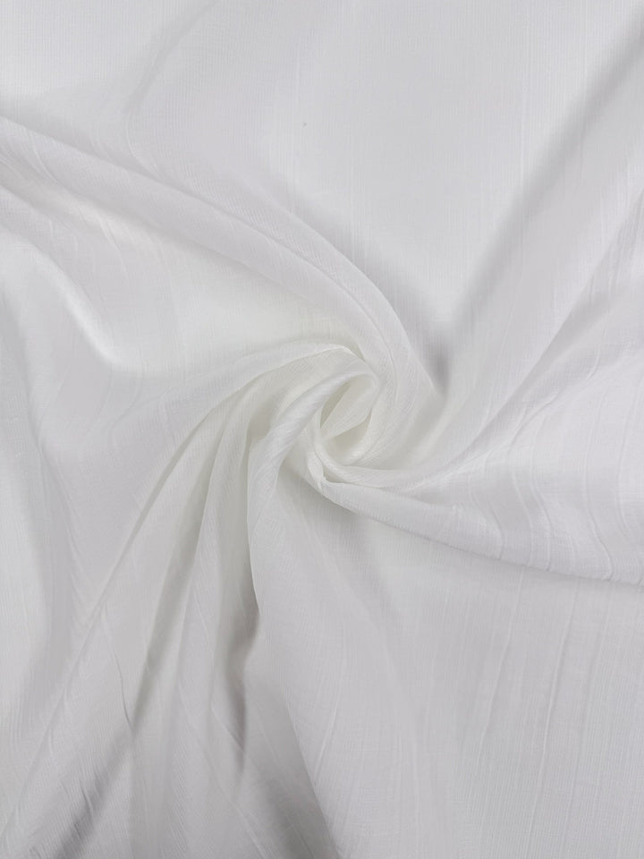 A close-up of Super Cheap Fabrics’ Textured Designer Voile in Ivory (155cm), a lightweight cotton blend with a subtle textured pattern, gently gathered to showcase its soft folds and swirling lines.