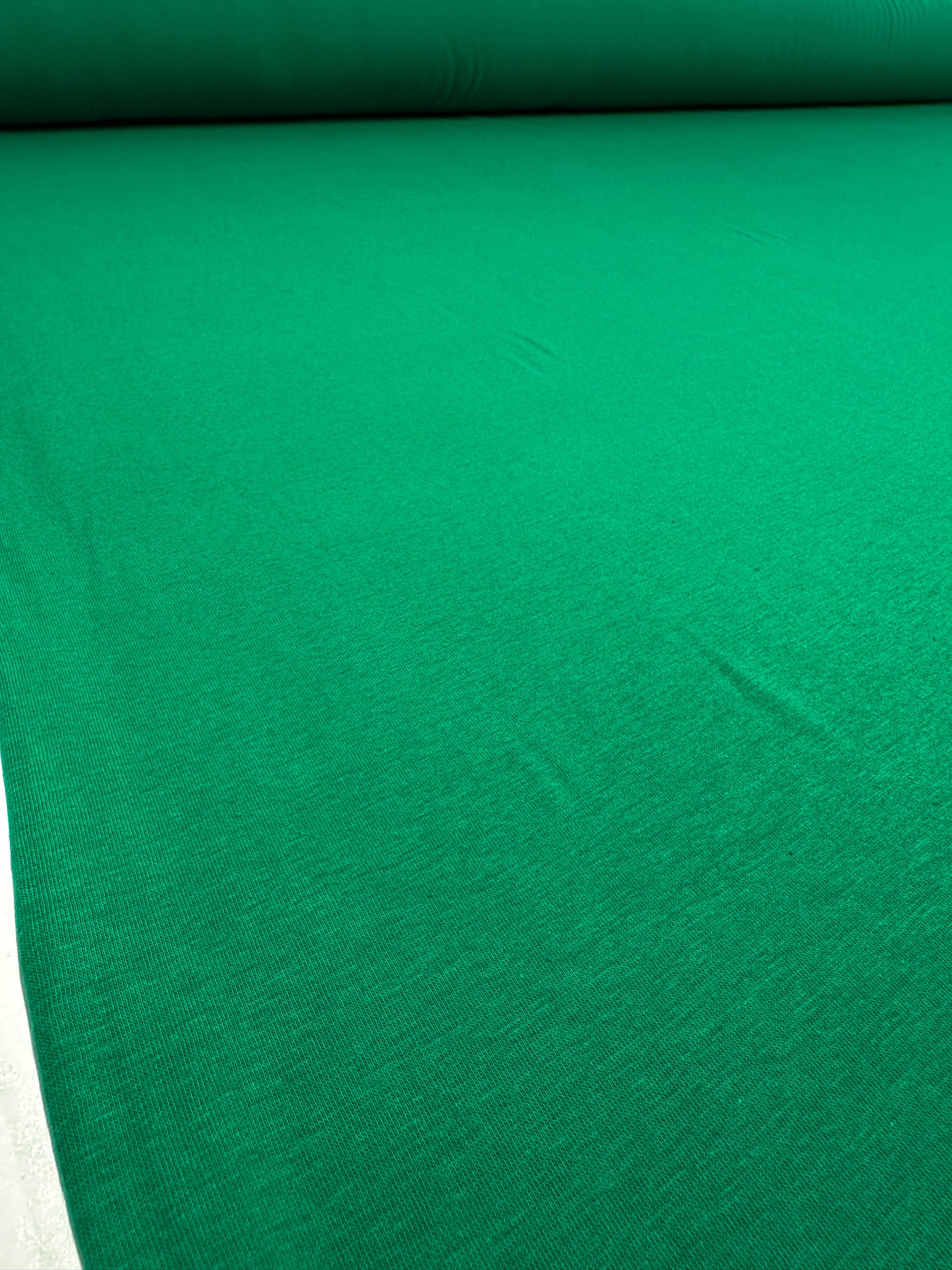 The Cotton Lycra - Green Tambourine by Super Cheap Fabrics is spread out, flaunting a smooth texture. Ideal for crafting sleek bodycon dresses, this 160cm stretch fabric offers both comfort and style.