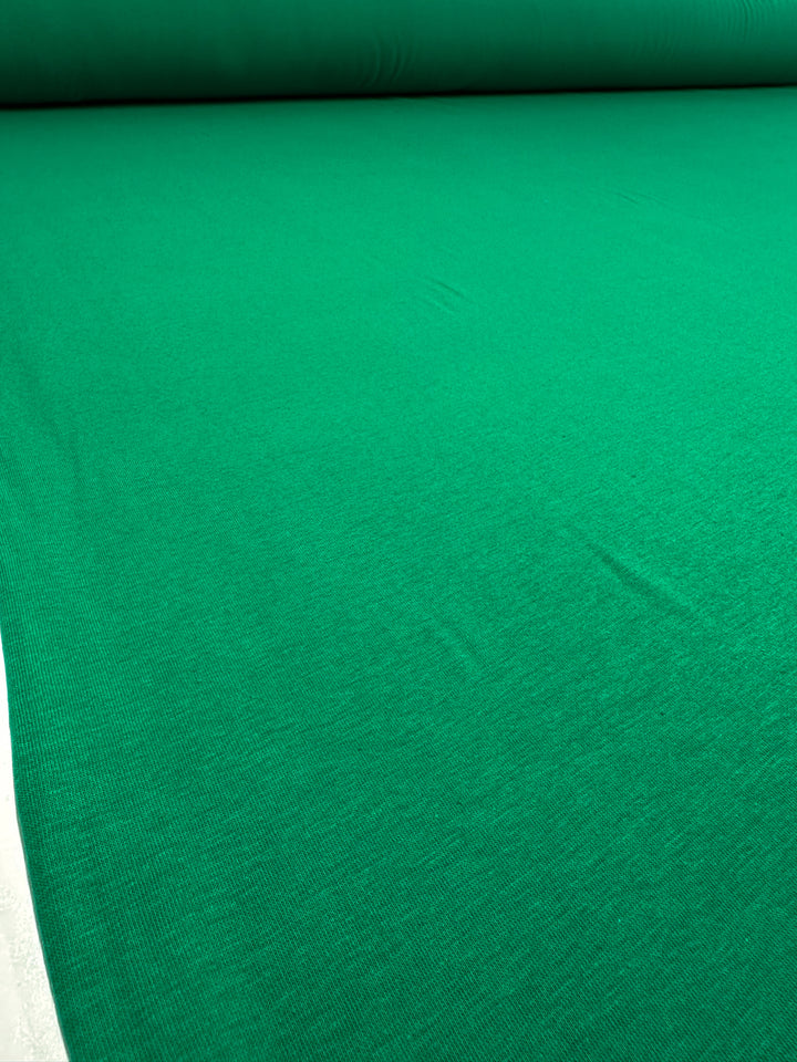 The Cotton Lycra - Green Tambourine by Super Cheap Fabrics is spread out, flaunting a smooth texture. Ideal for crafting sleek bodycon dresses, this 160cm stretch fabric offers both comfort and style.