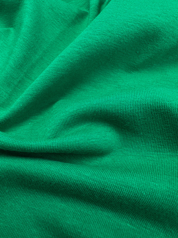 A close-up of Super Cheap Fabrics' Cotton Lycra in Green Tambourine, 160cm wide, reveals its vibrant textured surface. Gathered into soft folds, it showcases flexibility and drape perfect for bodycon dresses. Lighting highlights the weave beautifully.