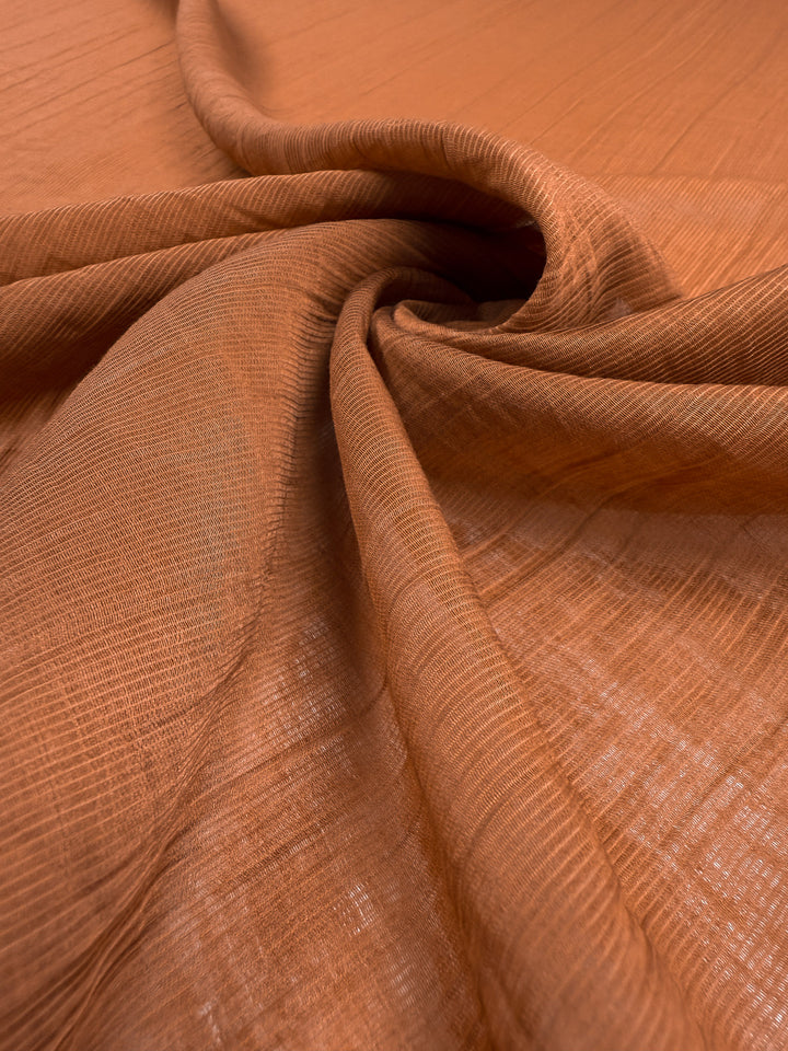 Close-up of Super Cheap Fabrics’ Textured Designer Voile in Rust (155cm), showing its soft, lightweight cotton nylon blend in gentle folds and swirl, highlighting the fabric’s delicate texture and slight sheerness.