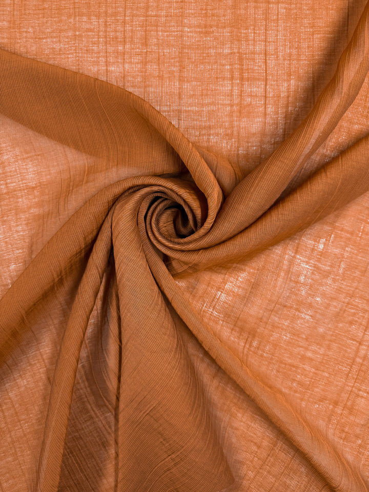 Textured Designer Voile - Rust by Super Cheap Fabrics features a fine, semi-transparent weave with a brown spiral pattern, highlighting the soft folds and lightweight texture of this 155cm wide fabric.