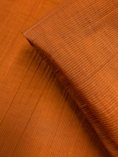 Close-up of Super Cheap Fabrics’ Textured Designer Voile in Rust (155cm): an orange cotton-nylon blend with fine parallel lines, smooth texture, and a detailed weave, shown with one layer neatly folded over another.