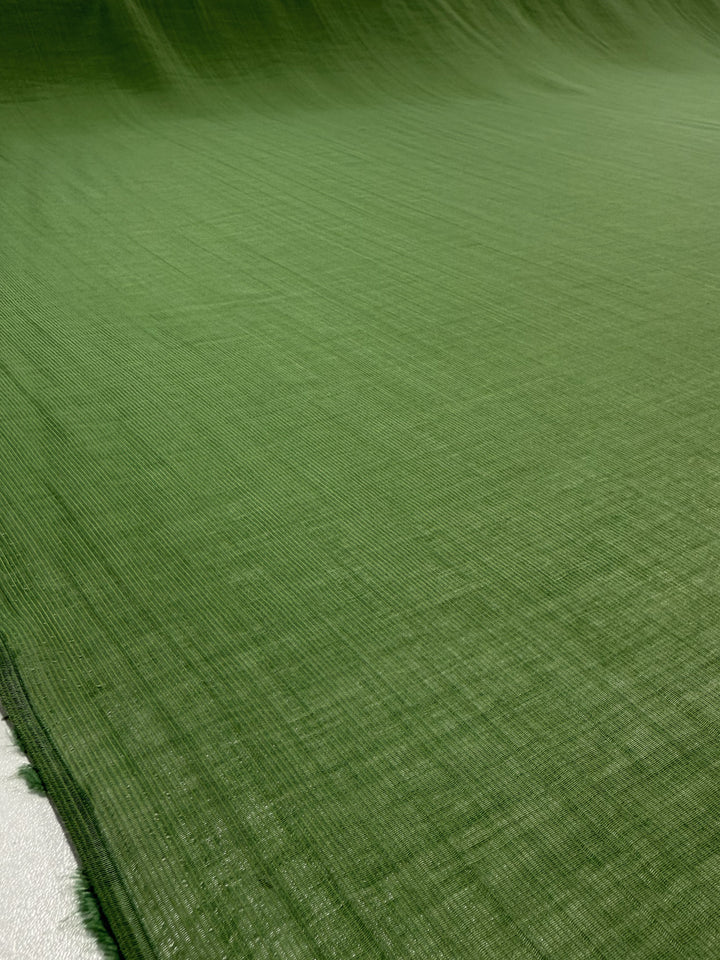 A close-up of Super Cheap Fabrics’ Textured Designer Voile - Salted Lime (155cm) shows its lightweight, slightly sheer green material with subtle horizontal lines, smoothly spread out to highlight its fine designer texture.