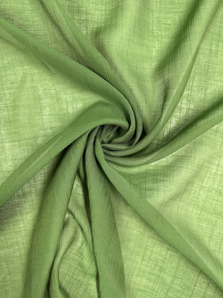 Close-up of Super Cheap Fabrics’ Textured Designer Voile in Salted Lime (155cm), showing its light green, translucent cotton-nylon blend, gathered and twisted to reveal the fine weave and unique texture.