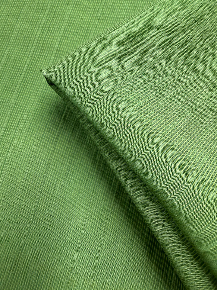 Close-up of Super Cheap Fabrics' Textured Designer Voile - Salted Lime (155cm), featuring green fabric with fine, horizontal light green pinstripes and a section of this lightweight summer material folded over.