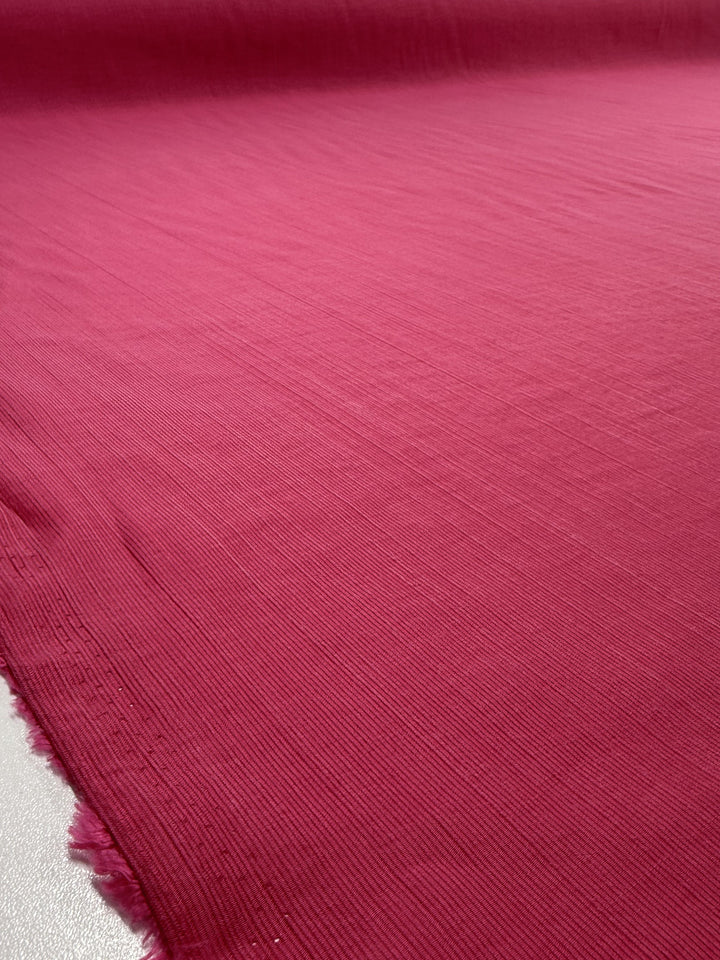 A close-up of Super Cheap Fabrics’ Textured Designer Voile in Raspberry Sorbet (155cm) shows its lightweight feel, fine horizontal lines, and slightly frayed edge.