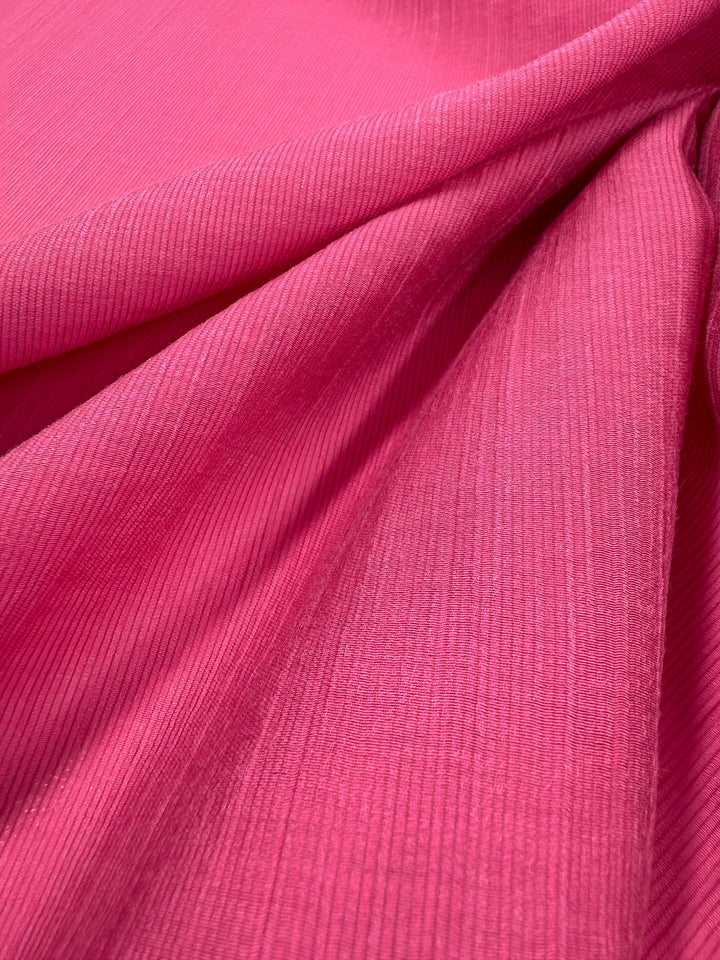 Close-up of Super Cheap Fabrics’ Textured Designer Voile in Raspberry Sorbet (155cm), featuring bright pink ribbed lightweight fabric with soft folds and diagonal textured lines.