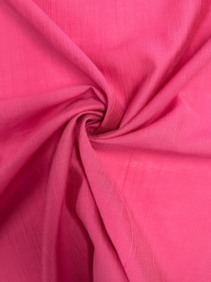 Super Cheap Fabrics' Textured Designer Voile in Raspberry Sorbet (155cm) features lightweight fabric with fine vertical lines, gathered and twisted at the center for soft folds and a swirling textured pattern.