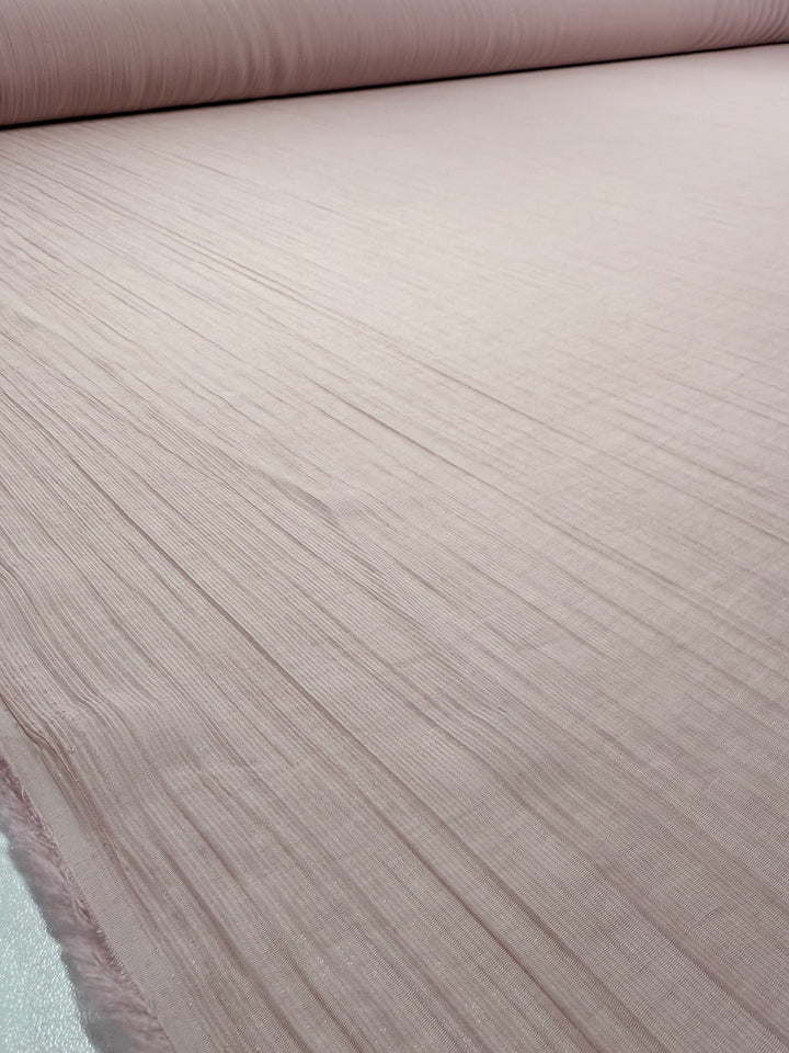 Super Cheap Fabrics’ Textured Designer Voile - Sepia Rose (155cm) features soft, lightweight cotton in light pink with subtle horizontal lines—ideal for airy summer dresses.