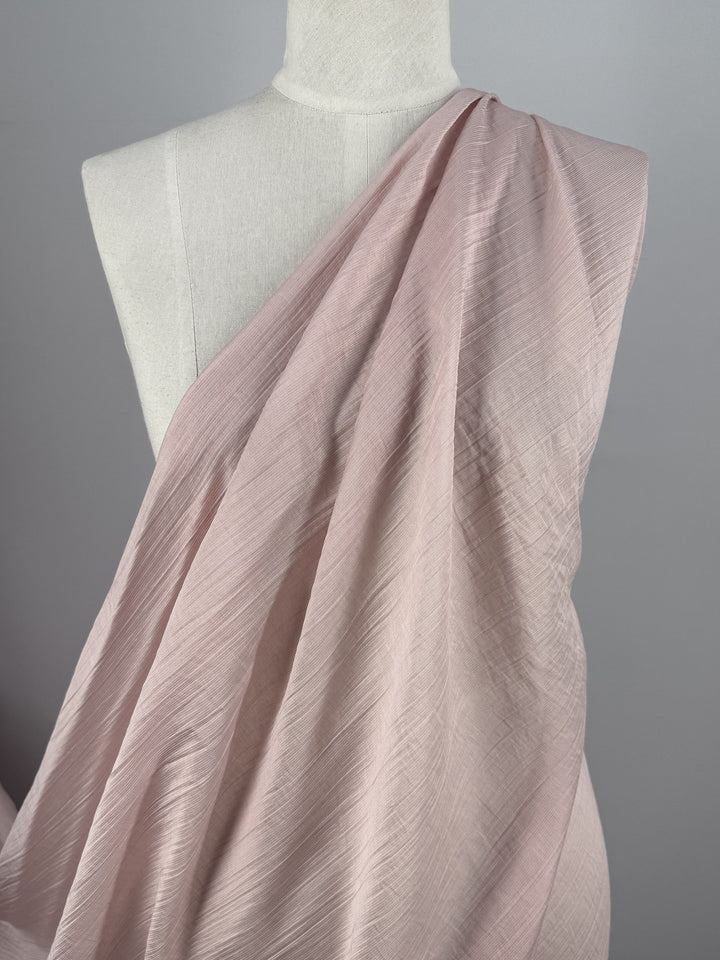 A close-up of a mannequin with Super Cheap Fabrics' Textured Designer Voile - Sepia Rose (155cm) draped diagonally over one shoulder, set against a plain gray background.