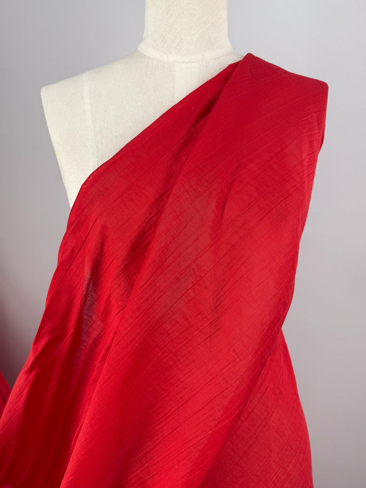 A white mannequin displays Super Cheap Fabrics' Textured Designer Voile - True Red (155cm) draped over one shoulder, set against a plain light gray background.