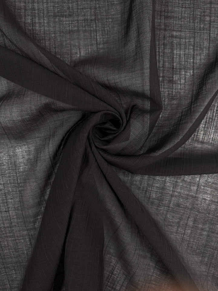 Super Cheap Fabrics' Textured Designer Voile - Black - 155cm features sheer black fabric arranged in spirals, creating soft folds and shadows across its textured surface.