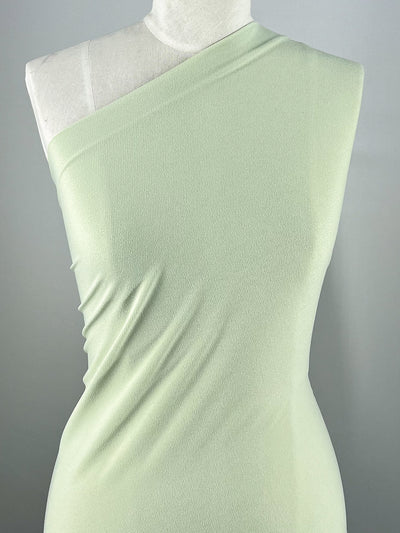 A mannequin showcases a single-shoulder, form-fitting dress in pistachio using medium weight jersey Crepe Lycra from Super Cheap Fabrics (148cm), with its sleek design elegantly highlighted against a neutral background.