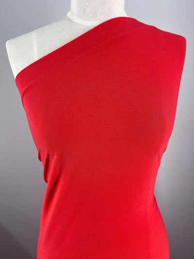 A mannequin dons a bright orange one-shoulder garment made from sleek Crepe Lycra - Tangelo by Super Cheap Fabrics. The smooth, fitted fabric covers the left shoulder, leaving the right exposed against a plain gray background.