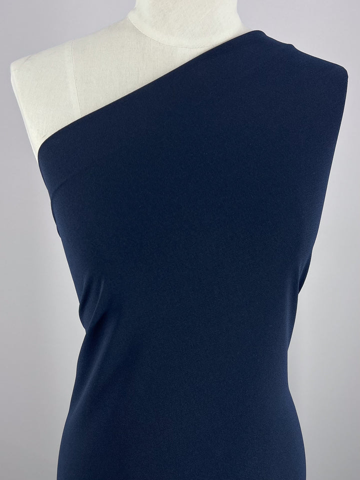 A mannequin wears a chic, dark blue, one-shoulder asymmetrical dress made from Super Cheap Fabrics' Crepe Lycra - Ink - 148cm, set against a simple backdrop.