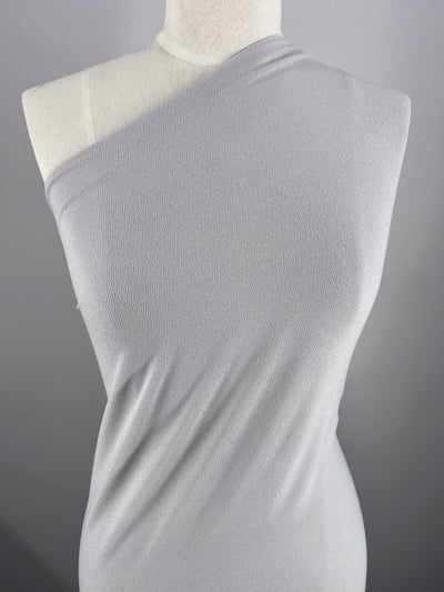 A mannequin wears a one-shoulder dress made from Super Cheap Fabrics' Crepe Lycra in Smoke. This medium weight jersey fabric drapes elegantly, its simple design contrasting beautifully against a plain grey background.