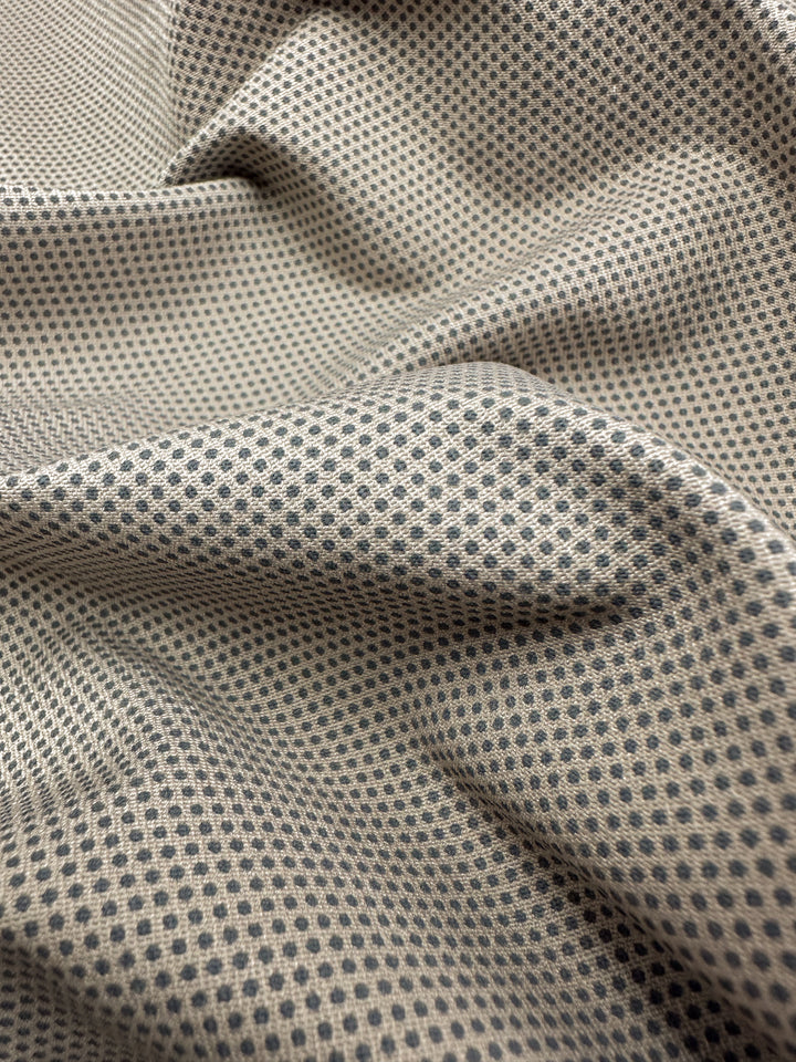 Close-up of the Printed Bengaline - Pin Dot Sand by Super Cheap Fabrics. This medium-weight stretch fabric, featuring a small black polka dot on beige, is gently draped to create soft folds and shadows that enhance its pattern's detail, offering structure and comfort. Width: 150cm.