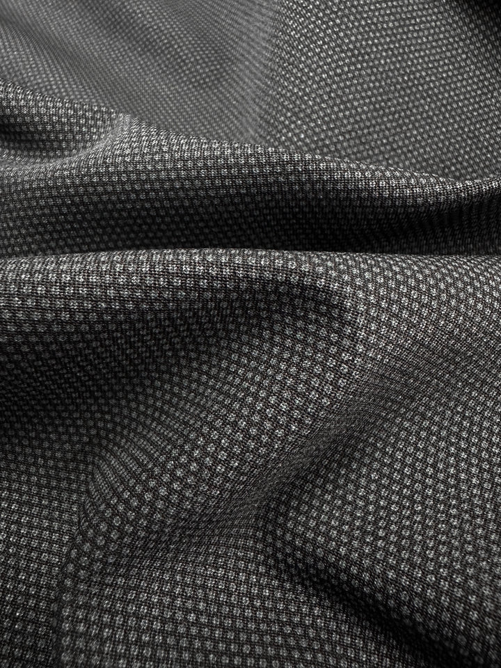 The Printed Bengaline - Pin Dot Black from Super Cheap Fabrics, measuring 150cm, is a medium-weight fabric in shades of gray and black with a small checkered pattern. Its soft texture, slight crumpling, and subtle highlights make it ideal for skirts and dresses.