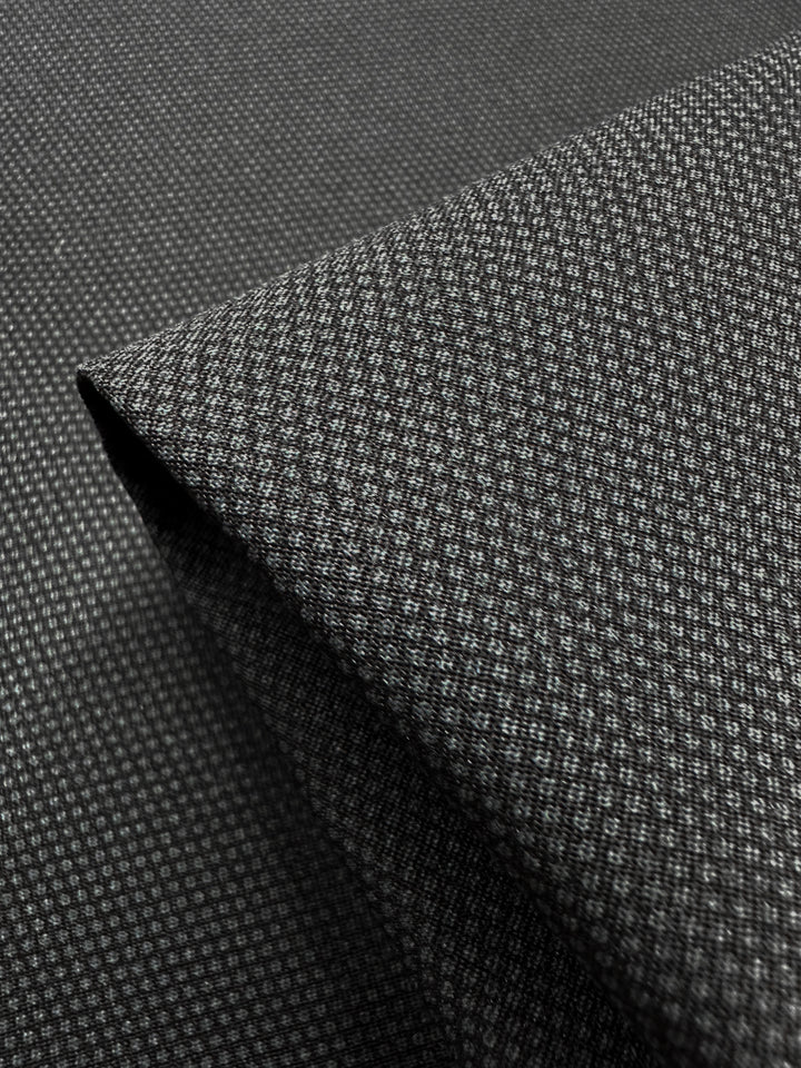 A close-up of folded Printed Bengaline - Pin Dot Black fabric by Super Cheap Fabrics, ideal for skirts and dresses. The medium-weight texture appears soft, revealing the detailed weave design. Width: 150cm.