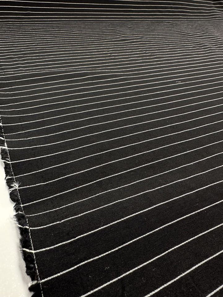 A close-up of Super Cheap Fabrics' Printed Bengaline in Ivory Pin Stripe showcases its subtle texture with thin, evenly spaced horizontal pinstripes on medium-weight black fabric. This 145cm stretch material is ideal for crafting skirts, dresses, pants, shorts, and jackets.