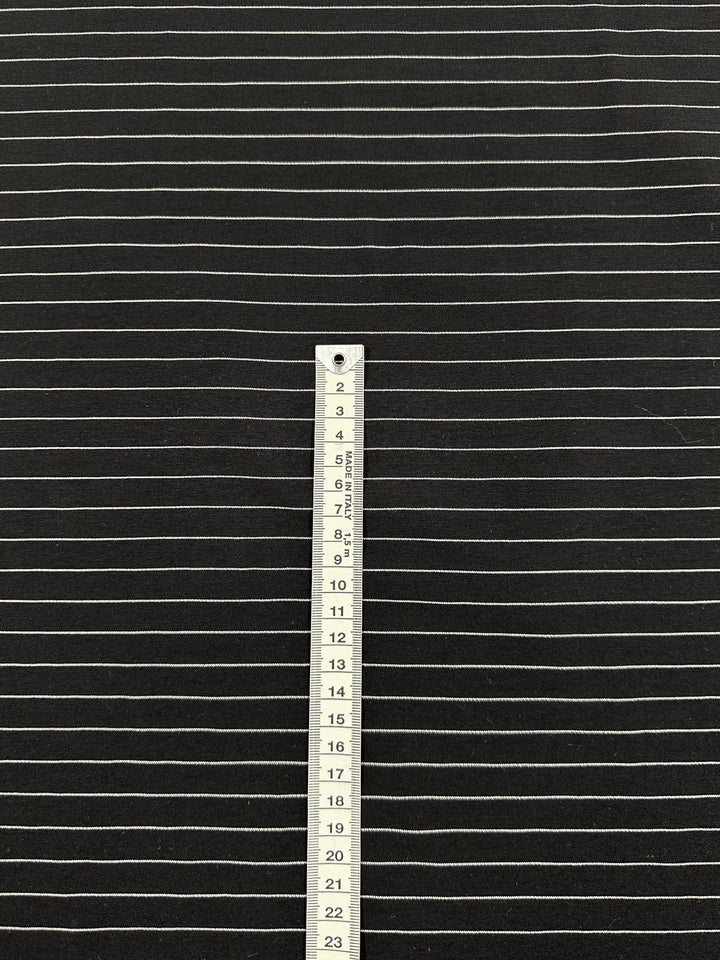 The Printed Bengaline - Ivory Pin Stripe from Super Cheap Fabrics features a black medium-weight, stretch fabric with thin white horizontal stripes and a vertical tape measure reaching 14 inches—ideal for crafting stylish skirts or pants with a sleek fit. Width: 145cm.