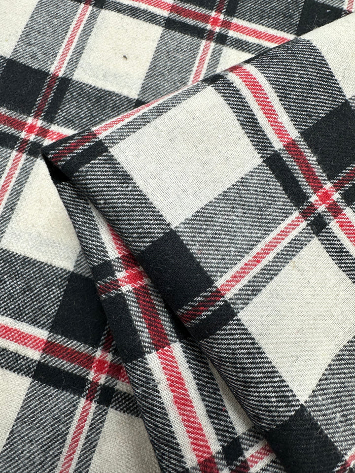 Close-up of Super Cheap Fabrics' Suiting - Black Watch Plaid (147cm), showing the folded cotton polyester fabric with a textured twill weave and intersecting black, white, gray, and red plaid lines.