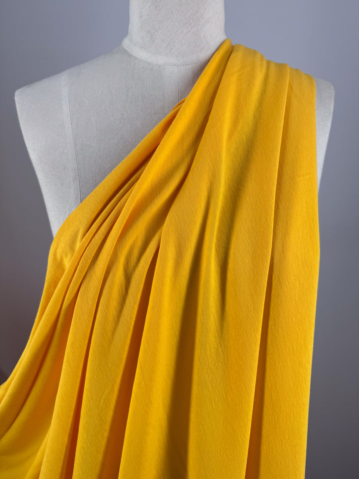 A mannequin elegantly wears a vibrant toga made of "Citrus" Cotton Jersey by Super Cheap Fabrics against a gray backdrop. The lightweight jersey, 155cm wide, drapes beautifully.
